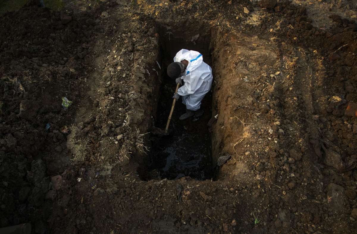Ein Mann im Schutzanzug hebt im indischen Gauhati Erde aus, um die Leiche einer Person zu begraben, die an Covid-19 gestorben ist.