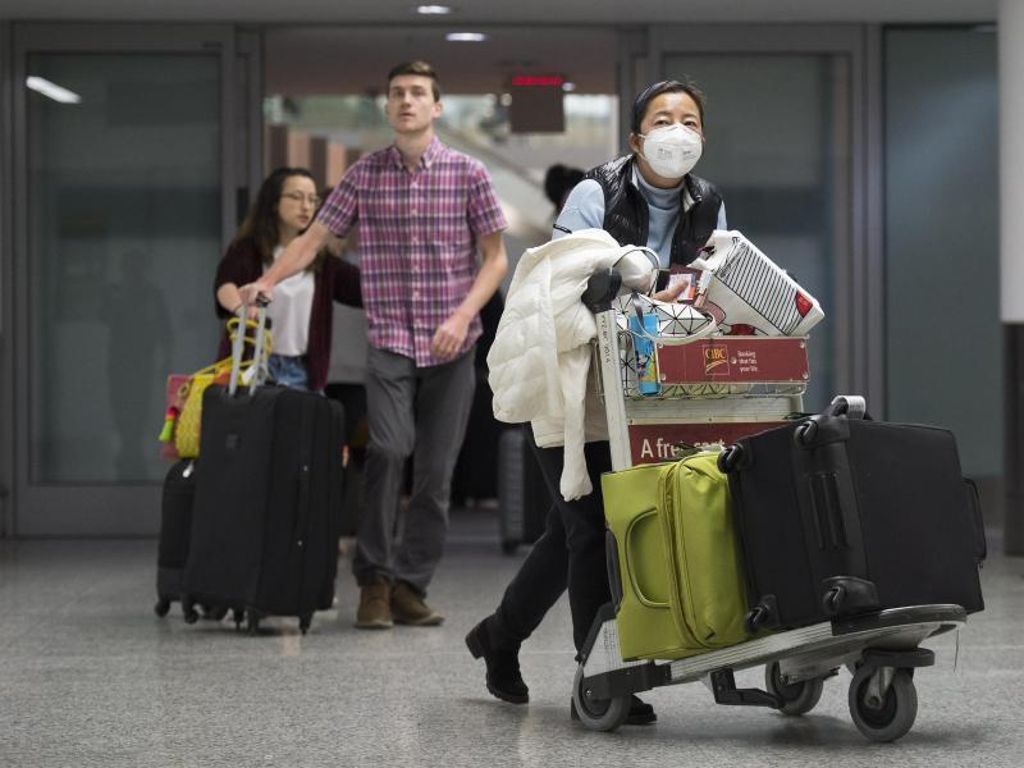 Eine Frau trägt am Toronto Pearson International Airport eine Atemschutz-Maske. Immer mehr Länder prüfen eine Evakuierung ihrer Landsleute. Foto: Nathan Denette/The Canadian Press/AP/dpa