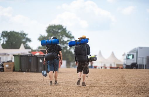 Zwei Festivalbesucher gehen mit ihrem Reisegepäck über das Wacken Open Air Festival. Foto: dpa/Daniel Reinhardt