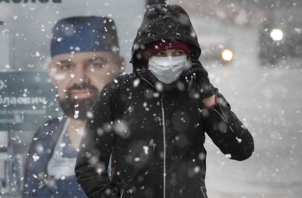 Im russischen St. Petersburg ist es dieser Tage deutlich kälter als hierzulande. Hier geht ein Mann mit Mundschutz an einem Poster vorbei, auf dem ein Arzt und ein Aufruf Zuhause zu bleiben abgebildet ist.